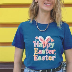 May include: A teal blue t-shirt with the words "Happy Easter. Easter" embroidered in pastel colours. The design includes bunny ears and hearts. The shirt is short-sleeved.