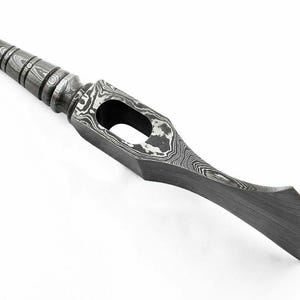 May include: A metal tool head featuring a pointed, ribbed spike on one end and a curved, flat blade on the other. The surface displays a distinct, swirling gray and black Damascus steel pattern with a central rectangular opening for a handle.