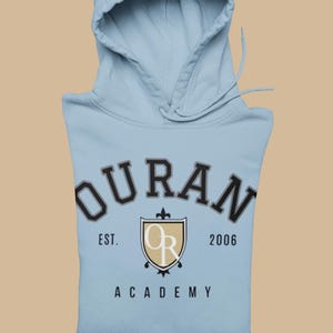 Puede incluir: Una sudadera con capucha de color azul claro que presenta el texto OURAN ACADEMY en una fuente oscura arqueada. Debajo del texto hay un emblema de escudo con las letras OR en blanco, flanqueado por el texto EST. y 2006 en una fuente negra sencilla.