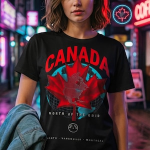 Könnte beinhalten: Ein schwarzes T-Shirt mit kurzen Ärmeln und einem großen roten Ahornblatt-Motiv, über dem das Wort CANADA in roten Buchstaben steht. Das Design umfasst ein blaues Globus-Gitter, den Text NORTH OF THE GRID sowie die Städtenamen TORONTO, VANCOUVER und MONTREAL.