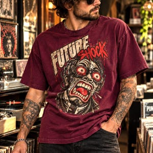 Könnte beinhalten: Ein kastanienbraunes Kurzarm-T-Shirt mit einem Grafikdruck eines schreienden Cyborgs, der eine Schutzbrille mit roten Gläsern trägt. Der Text FUTURE SHOCK ist in einer abgenutzten weißen und roten Schrift über dem Kopf abgebildet.