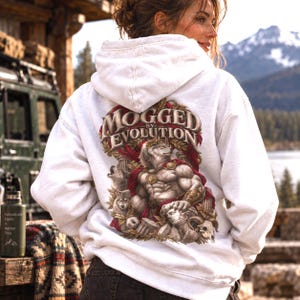 May include: A white hooded sweatshirt featuring a large graphic on the back. The design depicts a muscular anthropomorphic wolf figure in a Roman-style cape and laurel wreath, surrounded by smaller wolves, columns, and the text MOGGED BY EVOLUTION.