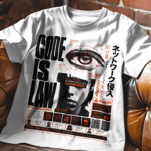 Könnte beinhalten: Ein weißes Kurzarm-T-Shirt mit einem schwarz-roten Grafikdruck. Das Design zeigt den Text "CODE IS LAW", ein großes Auge, ein Gesicht mit einem Zensurbalken, japanische Schriftzeichen sowie verschiedene technische Interface-Elemente.