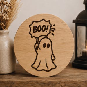 May include: A round wooden Halloween decoration featuring a ghost holding a sign that says "BOO!". The ghost and text are etched in black on the light brown wood. The design is simple and festive, perfect for seasonal decor.