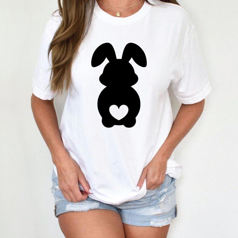 May include: White t-shirt featuring a black silhouette of a bunny with a heart-shaped detail. The bunny design is centered on the front of the shirt. The shirt has short sleeves and a crew neck.