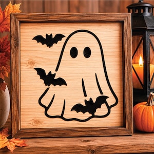 May include: Wooden Halloween sign featuring a black ghost and bats design. The artwork is set within a brown wooden frame. The background has a wood grain texture. The sign is a decorative item for the Halloween season.