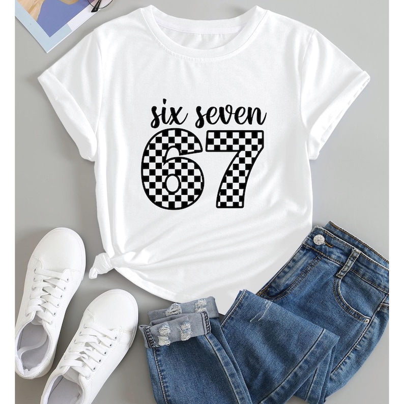 K&ouml;nnte beinhalten: Wei&szlig;es T-Shirt mit dem Text "six seven" &uuml;ber der Zahl "67". Die Zahlen sind schwarz-wei&szlig; kariert. Das Shirt wird mit einer blauen Jeans und wei&szlig;en Turnschuhen kombiniert. Ein l&auml;ssiges Outfit.