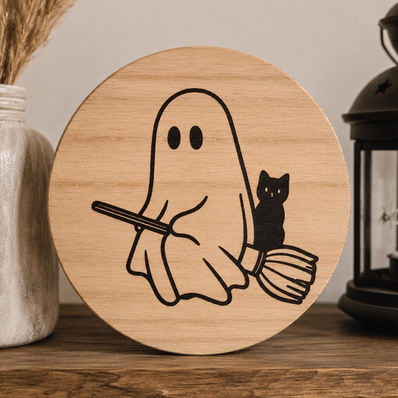 May include: A round wooden sign featuring a black illustration of a ghost riding a broom with a black cat. The ghost has two oval eyes. The sign is made of light-colored wood and is suitable for Halloween decor.