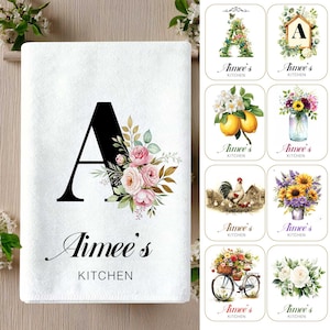 May include: A white rectangular kitchen towel featuring a large black letter A decorated with pink roses and green leaves, with the text Aimee's KITCHEN printed below. To the right are eight smaller rectangular designs with various floral and farm motifs.