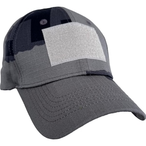 Może przedstawiać: Szara czapka bejsbolowa z kamuflażem i kwadratową, jasnoszarą naszywką z przodu. Czapka ma zakrzywiony daszek i jest wykonana z wytrzymałej tkaniny. Odpowiednia do aktywności na świeżym powietrzu i noszenia na co dzień.