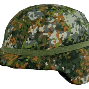 Puede incluir: Un casco con patrón de camuflaje con una banda verde. El casco presenta una mezcla de colores verdes, marrones, grises y blancos. El borde del casco es ligeramente curvado y se ven las orejeras.
