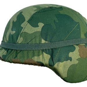 Puede incluir: Un casco de camuflaje verde con forma redondeada y ala. El casco presenta un patrón de formas verdes, marrones y beige. Una banda verde oscuro rodea el casco cerca del ala.