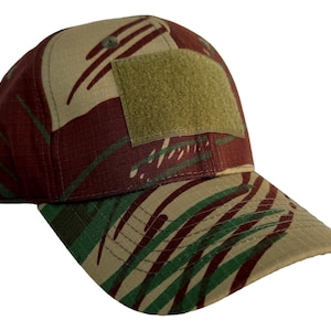 Puede incluir: Gorra de béisbol de camuflaje en tonos marrón, verde y beige. La gorra presenta un parche cuadrado en la corona y una visera curva. El patrón se asemeja a rayas de tigre.