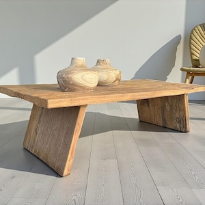 K&ouml;nnte beinhalten: Ein rustikaler, rechteckiger Couchtisch aus Holz mit nat&uuml;rlicher Oberfl&auml;che. Zwei dekorative Holzvasen stehen auf der Tischoberfl&auml;che. Der Tisch hat abgewinkelte Beine und steht auf einem hellen Holzboden.