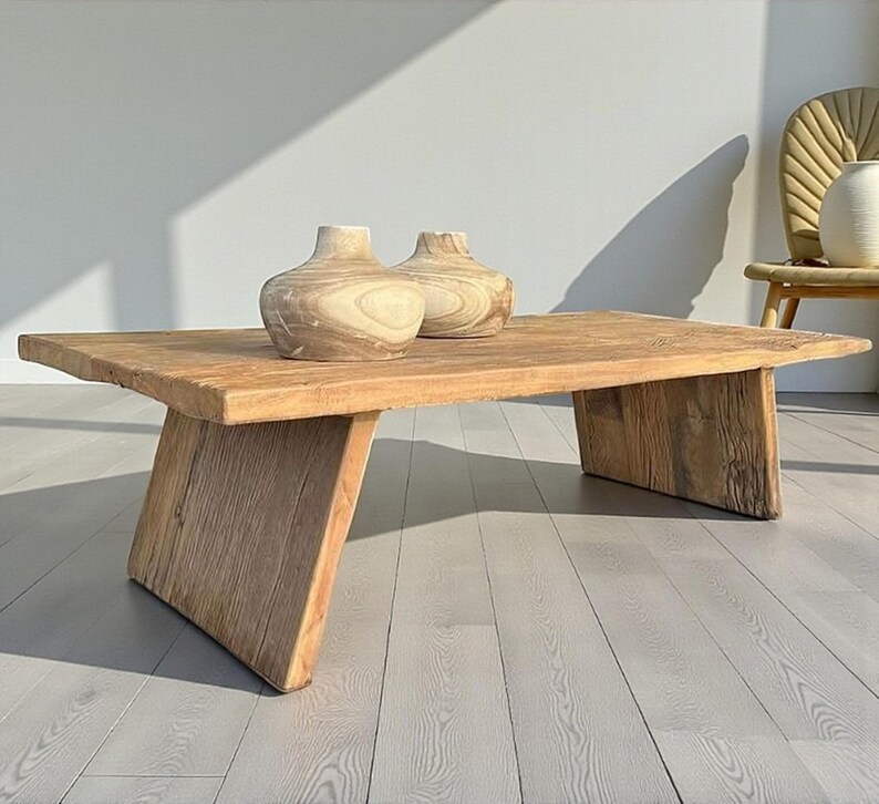 K&ouml;nnte beinhalten: Ein rustikaler, rechteckiger Couchtisch aus Holz mit nat&uuml;rlicher Oberfl&auml;che. Zwei dekorative Holzvasen stehen auf der Tischoberfl&auml;che. Der Tisch hat abgewinkelte Beine und steht auf einem hellen Holzboden.