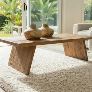 K&ouml;nnte beinhalten: Ein rechteckiger Couchtisch aus hellem Holz mit schr&auml;gen Beinen. Zwei dekorative Vasen stehen auf der Tischoberfl&auml;che. Der Tisch ist aus hellbraunem Holz gefertigt und steht auf einem wei&szlig;en Teppich. Der Hintergrund umfasst ein Sofa und gro&szlig;e Fenster.