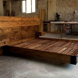 May include: A handcrafted wooden bed frame with a headboard and integrated nightstands. The bed features a rich, dark wood grain finish. The headboard has a curved top and the bed frame is supported by black corner posts. The bed frame measures approximately 80 inches long.