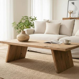 K&ouml;nnte beinhalten: Ein rustikaler Couchtisch aus Holz mit nat&uuml;rlicher Oberfl&auml;che. Im Hintergrund befindet sich ein beiges Sofa mit Kissen. Eine Holzvase, ein Buch sowie eine Tasse und Untertasse stehen auf dem Tisch. Der Raum ist von nat&uuml;rlichem Licht durchflutet.