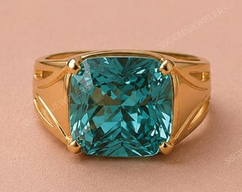 May include: A gold ring featuring a large, cushion-cut, teal-colored gemstone set in a four-prong mounting. The band has a smooth, polished finish with decorative cut-out details on the sides, showcasing a vibrant, faceted center stone.