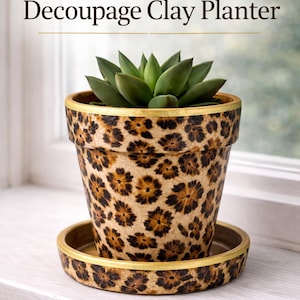May include: A decoupage clay planter with a leopard print design. The planter has a gold rim and matching saucer. The planter holds a green succulent plant. Text on the image reads "Leopard Print Decoupage Clay Planter."