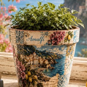 May include: A ceramic plant pot featuring a decorative collage print of the Amalfi coast, including a coastal town, blue sea, yellow lemons, and pink flowers. The word Amalfi is printed in blue script on the upper rim, surrounded by tile patterns.