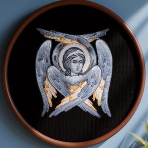 May include: A cross-stitch artwork of an angel with outstretched wings, set in a round wooden frame. The angel features a serene expression, a halo, and detailed wings in shades of gray, blue, and gold against a black background. The text at the bottom reads "MOCKUP IMAGE FOR DISPLAY PURPOSES ONLY."