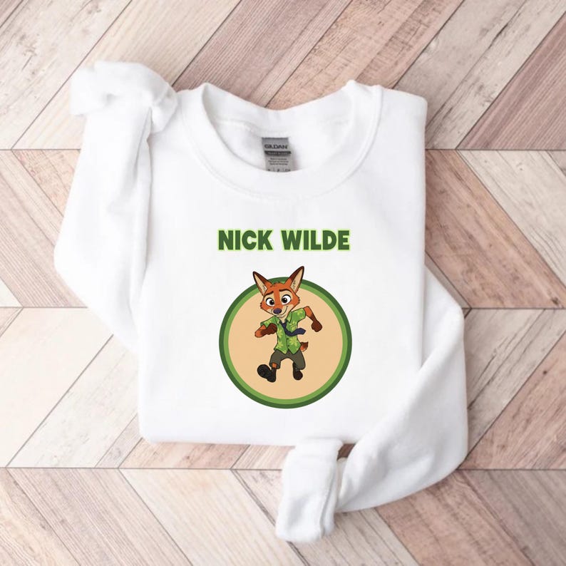May include: White sweatshirt featuring a cartoon image of Nick Wilde from Zootopia. The image shows Nick Wilde in a green shirt and tie, inside a green and tan circle. The words "NICK WILDE" are printed above the image in green.