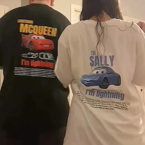 May include: Two t-shirts featuring characters from the movie Cars. One is black with a red Lightning McQueen graphic and the text "MCQUEEN". The other is white with a blue Sally graphic and the text "I'm Sally".