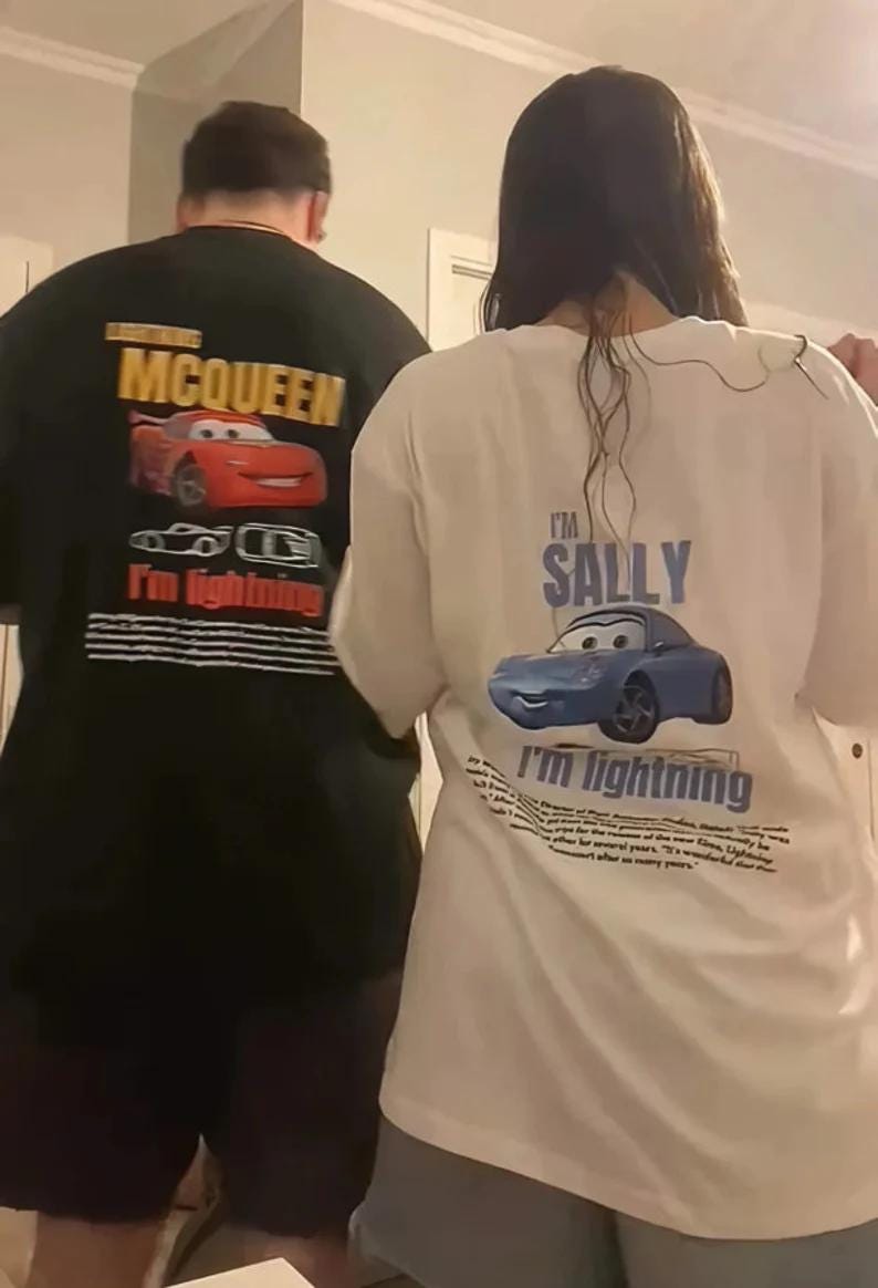 May include: Two t-shirts featuring characters from the movie Cars. One is black with a red Lightning McQueen graphic and the text "MCQUEEN". The other is white with a blue Sally graphic and the text "I'm Sally".