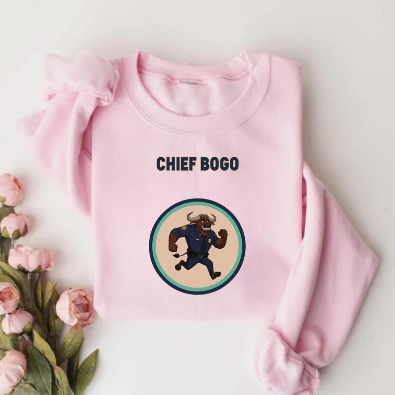 May include: A light pink sweatshirt with the text "CHIEF BOGO" above a circular graphic. The graphic features a cartoon bull in a police uniform running. The bull is brown and wearing a blue uniform.