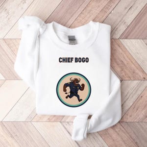 May include: White sweatshirt with the text "CHIEF BOGO" above a circular graphic. The graphic features a cartoon bull in a police uniform running. The bull is brown with a blue uniform and a badge.