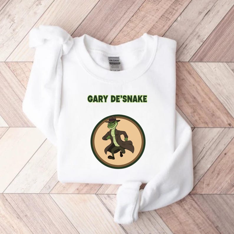 May include: White sweatshirt with the text "GARY DE'SNAKE" and a circular graphic of a cartoon snake in a trench coat and hat. The sweatshirt is made of a soft material. The design is printed on the front.