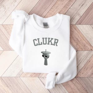 May include: A white ceramic mug with a black handle and the text "But First, Coffee" in a bold, black font. The mug is set against a blurred background, suggesting a cozy setting. The mug appears to be approximately 4 inches tall.