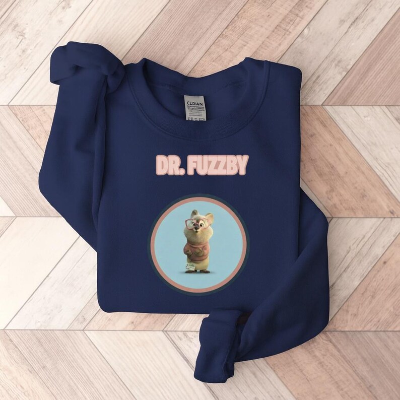May include: A navy blue sweatshirt with the text "DR. FUZZBY" in pink above a circular graphic. The graphic shows a cartoon character wearing glasses and a sweater. The sweatshirt is made of a soft material.