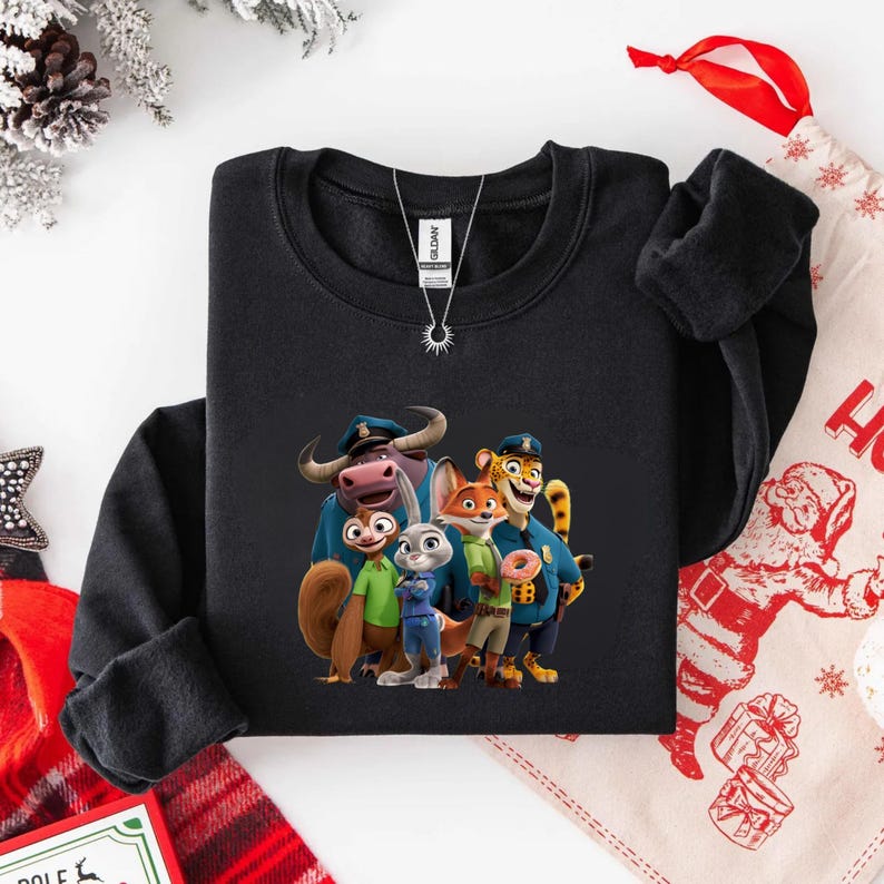 Puede incluir: Sudadera negra de cuello redondo con un gr&aacute;fico colorido de personajes de la pel&iacute;cula animada Zootopia. El dise&ntilde;o incluye a Judy Hopps, Nick Wilde y otros personajes con sus uniformes de polic&iacute;a. Se ve un collar plateado con un colgante de sol.