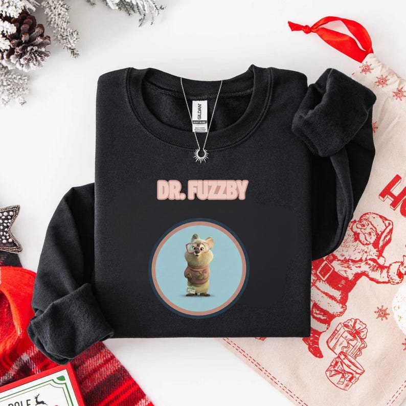 May include: Black sweatshirt with pink text reading "DR. FUZZBY". The sweatshirt displays a circular graphic of a cartoon character wearing glasses and a sweater. A silver necklace with a sun pendant is visible.