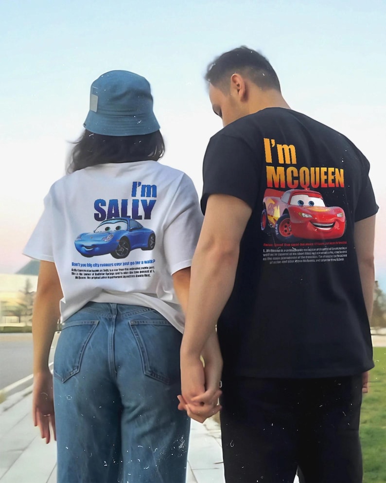 May include: White t-shirt with a blue cartoon car and the text "I'm SALLY". Black t-shirt with a red cartoon car and the text "I'm McQUEEN". The shirts are worn by two people holding hands.