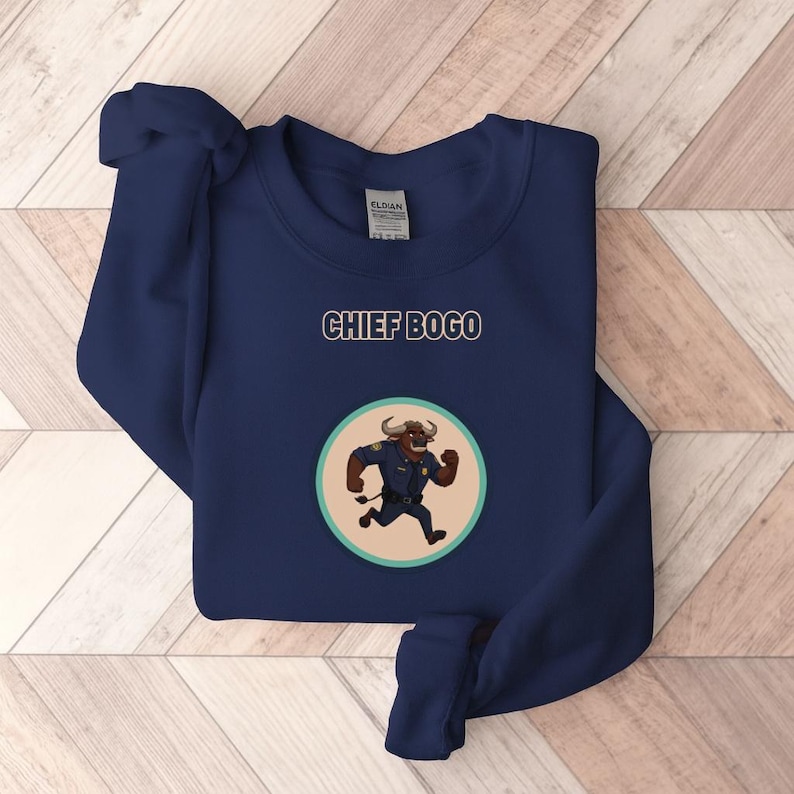 May include: Navy blue sweatshirt featuring the text "CHIEF BOGO" above a circular graphic. The graphic depicts a cartoon buffalo in a police uniform running. The sweatshirt is made of a soft material.
