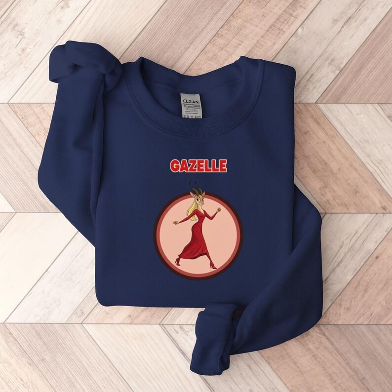 May include: A navy blue sweatshirt featuring the word "GAZELLE" in red above a cartoon gazelle in a red dress, within a pink circle. The gazelle has blonde hair and is wearing red heels.