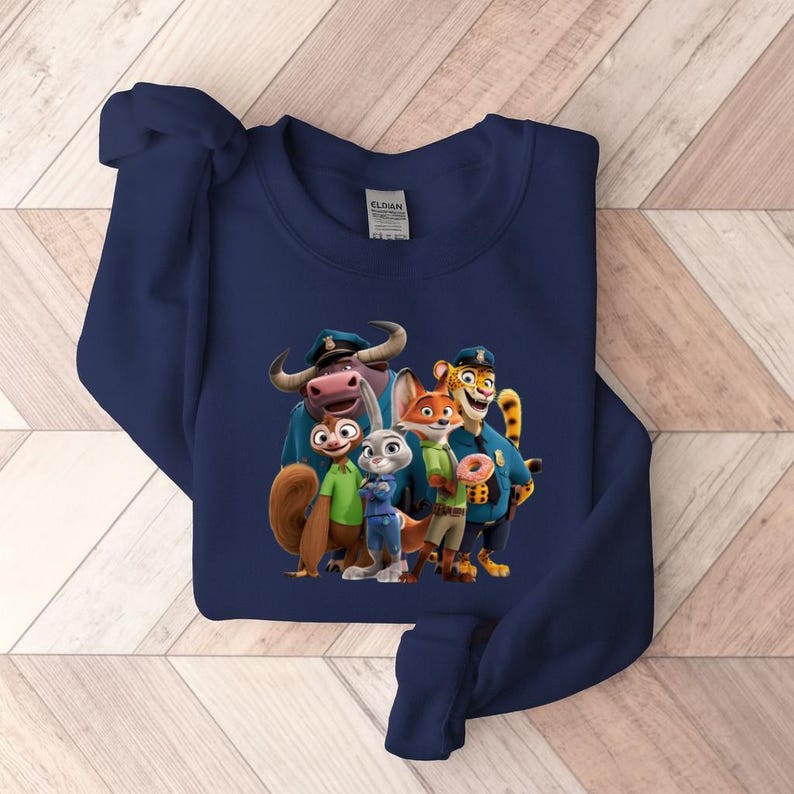 Puede incluir: Sudadera azul marino con un gr&aacute;fico colorido de personajes de la pel&iacute;cula animada Zootopia. El dise&ntilde;o incluye una ardilla, un conejo, un zorro, un tigre y un b&uacute;falo, todos con uniformes de polic&iacute;a. La sudadera es de material suave.