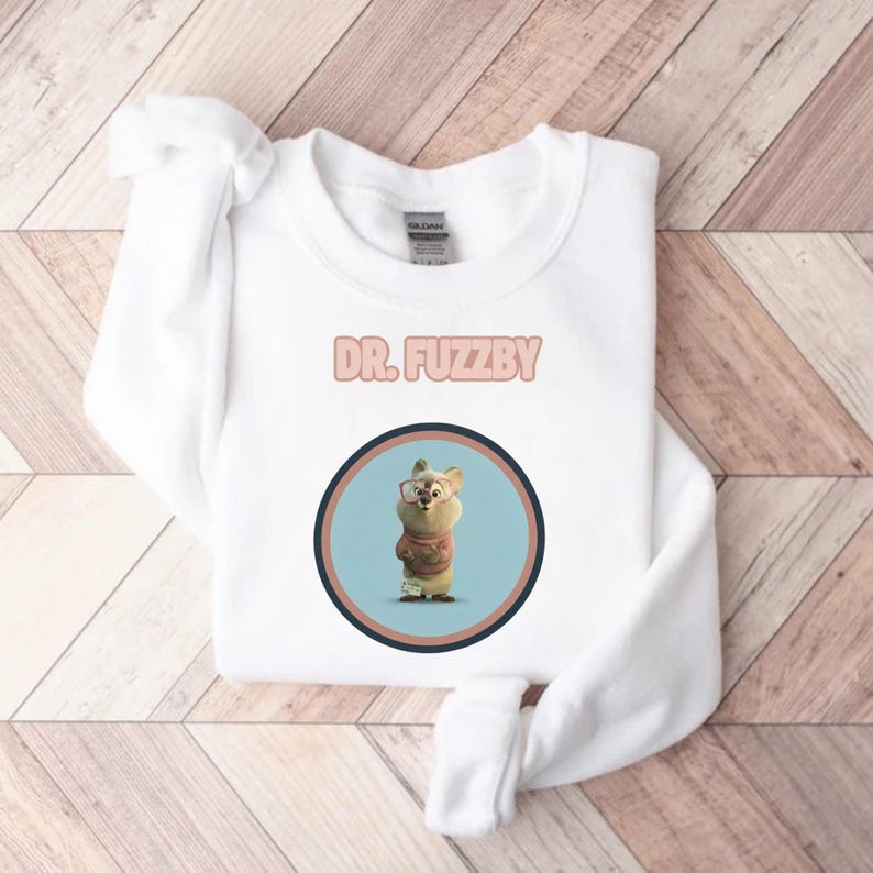 May include: White sweatshirt with the text "DR. FUZZBY" in pink. The sweatshirt features a circular graphic of a cartoon character wearing glasses and a sweater. The graphic is set against a light blue background.