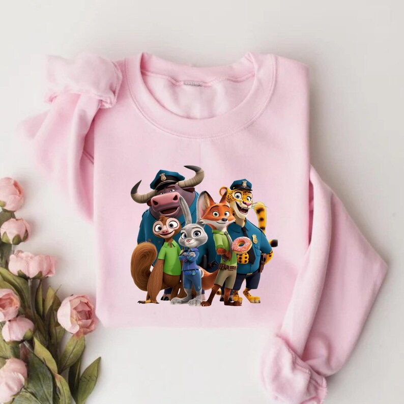 Puede incluir: Sudadera rosa claro con un estampado gr&aacute;fico de personajes de la pel&iacute;cula animada "Zootr&oacute;polis". El dise&ntilde;o presenta un b&uacute;falo, una ardilla, un conejo, un zorro y un guepardo con uniformes de polic&iacute;a. La sudadera tiene mangas largas.