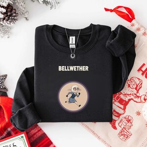 May include: Black sweatshirt with the word "BELLWETHER" in white block letters. Below the text is a circular graphic of a cartoon sheep wearing glasses and a blue suit. The sheep is running. A silver necklace is visible.