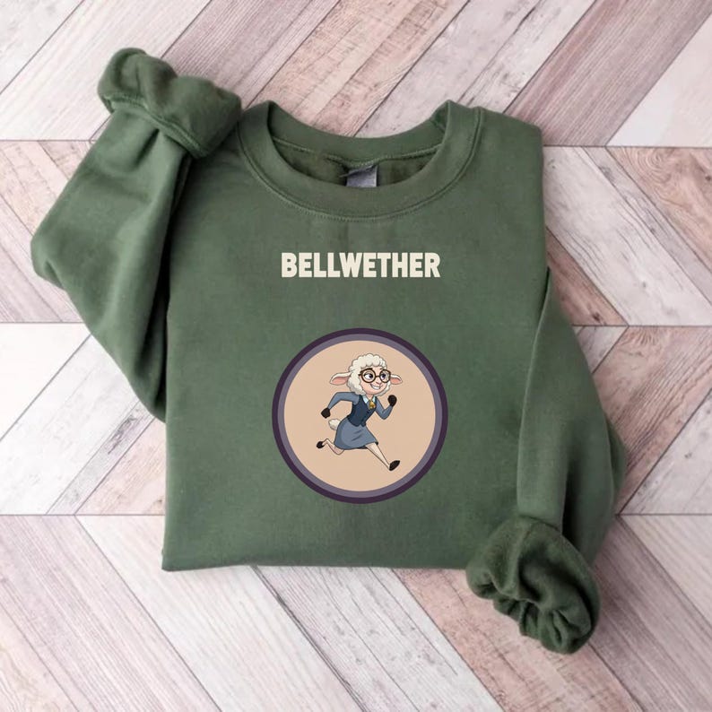 Op de afbeelding: Groen sweatshirt met het woord "BELLWETHER" in witte letters. Daaronder een cirkelvormige afbeelding van een schaap met een bril en een blauw pak, in een rennende pose. Het sweatshirt heeft lange mouwen.