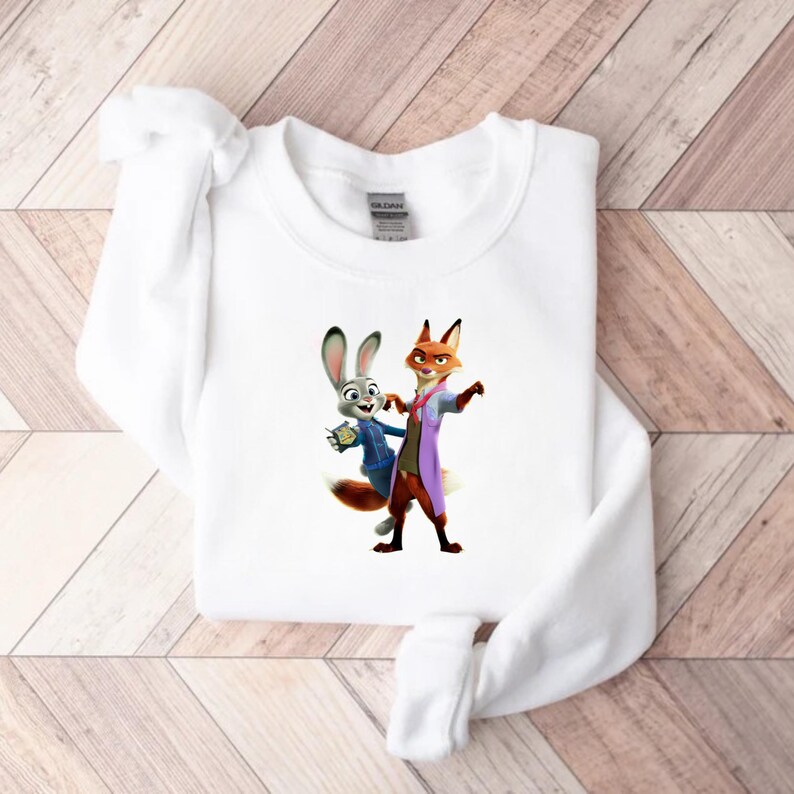 May include: White sweatshirt featuring a colorful graphic of two cartoon characters, a rabbit and a fox, in a friendly pose. The rabbit wears a blue jacket, and the fox wears a purple coat. The sweatshirt is made of a soft material.