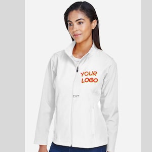 May include: A white softshell jacket with a full-length zipper and a stand-up collar. The jacket features the text "YOUR LOGO" in red. The model is wearing blue jeans.