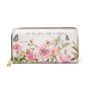 May include: White zippered wallet with a floral design featuring pink and peach flowers, butterflies, and the text "for his favor lasts a lifetime" and "psalm 30:5". The wallet has a gold zipper and pull.