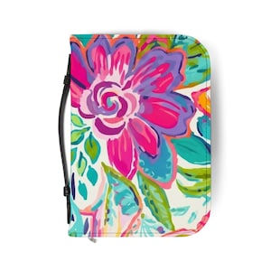 May include: A rectangular zippered organizer case featuring a vibrant floral pattern with large pink, purple, and teal blossoms against a white background. The case includes a black wrist strap attached to the side, providing a secure way to carry.