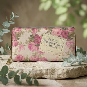 May include: A floral wallet featuring a beige backdrop and pink roses. The wallet has a gold zip and a patch with the text "BE STILL AND KNOW THAT I AM GOD" and "Psalm 46:10".