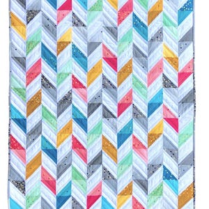 May include: A rectangular quilt with a chevron pattern in various colours. The quilt features white, grey, teal, pink, yellow, and gold. The quilt is made of fabric and has a quilted design. The quilt's dimensions are not specified, but it appears to be a standard size.